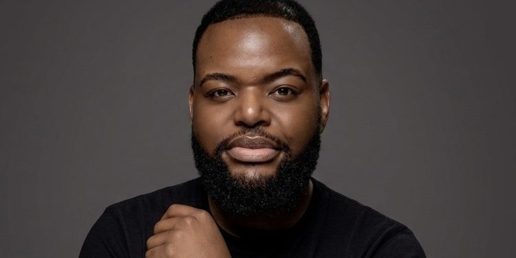 Head-and-shoulders portrait of a man with a beard in a black shirt against a gray backdrop.