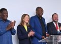 Four people stand at a podium, smiling and clapping after a presentation or press conference.