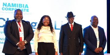 Four professionals on stage posing for a photo at a Namibia Corporate event, with a bright backdrop and branding visible behind them.