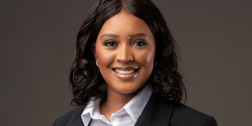 Professional headshot of a smiling woman in a black blazer and white shirt against a neutral backdrop.