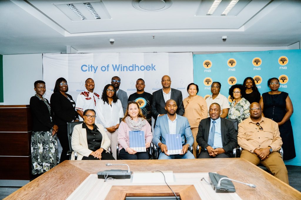 Group of men and women in business attire posing for a photo in a conference room; backdrop reads 'City of Windhoek'.