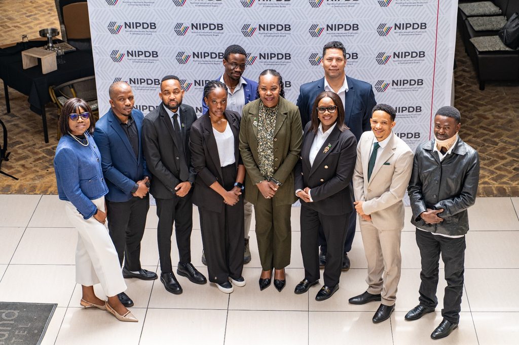Ten professionals stand together for a group photo at a NIPDB event, backdrop shows repeated NIPDB logos and branding.