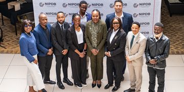 Ten professionals stand together for a group photo at a NIPDB event, backdrop shows repeated NIPDB logos and branding.