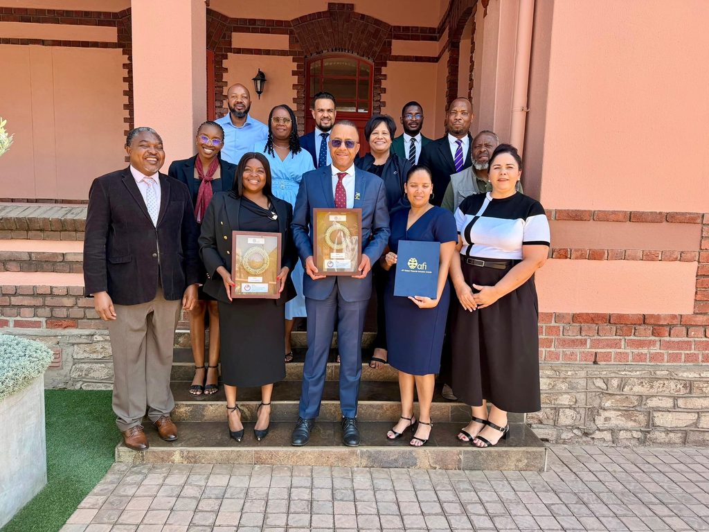 WhatsApp Image 2026-09-09 at 123731 PM - The Brief | Namibia's Leading Business & Financial News A group of professionals posing on steps outside a brick building, two people in front holding framed awards.