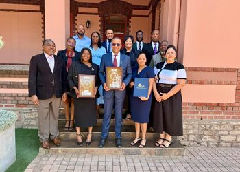 A group of professionals posing on steps outside a brick building, two people in front holding framed awards.