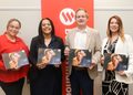 Four professionals pose together, each holding a 2026 Social Value Report booklet in front of a red banner with a white logo.