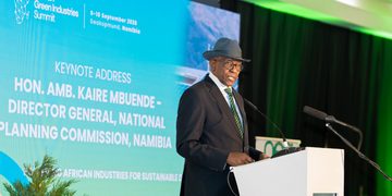 Speaker at a podium delivering the keynote at the African Green Industries Summit, with a blue screen behind him displaying event details