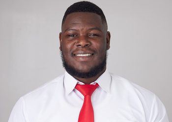 Smiling man in a white dress shirt and bright red tie, facing the camera against a light gray background.