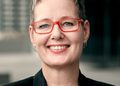 Eline-Van-Der-Linden - The Brief | Namibia's Leading Business & Financial News Smiling woman with short gray hair and red rectangular glasses, wearing a black blazer, outdoors near a modern building grounds.