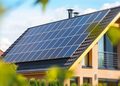 Modern brick house with a large solar panel array on the sloped roof under a blue sky.