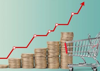 Stacked coins increasing in height beside a shopping cart, with a red upward growth line indicating rising value or costs.
