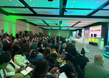 Large conference hall with a panel on stage and a crowded audience listening.