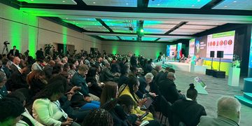 Large conference hall with a panel on stage and a crowded audience listening.
