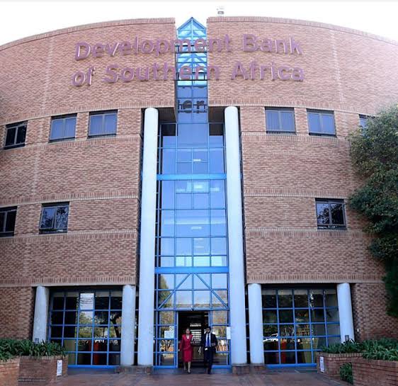 DEVELOPMENT BANK OF SOUTHERN AFRICA - The Brief | Namibia's Leading Business & Financial News Brick office building with a blue glass central entrance and two tall white pillars; two people stand at the doors under a Development Bank of Southern Africa sign.
