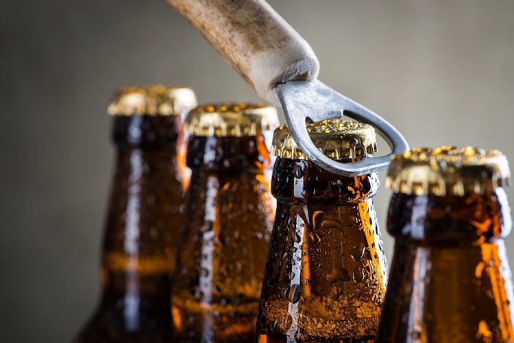 BEER1 - The Brief | Namibia's Leading Business & Financial News Beer bottles with caps being pried open by a metal bottle opener, close-up shot of condensation-streaked bottles in a row.