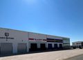 White industrial complex with three garage bays and signs for AUAS MOTORS and GLASFIT under a clear blue sky.