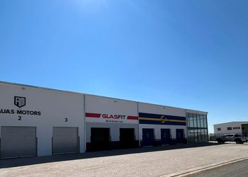 White industrial complex with three garage bays and signs for AUAS MOTORS and GLASFIT under a clear blue sky.
