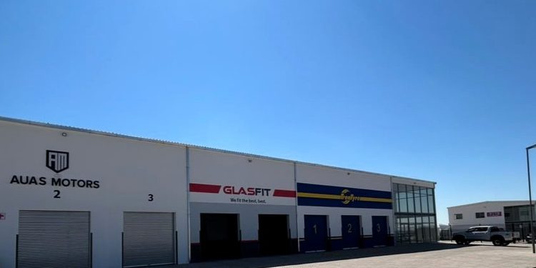 White industrial complex with three garage bays and signs for AUAS MOTORS and GLASFIT under a clear blue sky.