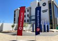 Modern corporate building with red Bank Windhoek and blue Capricorn Group flags in front of a clear sky.