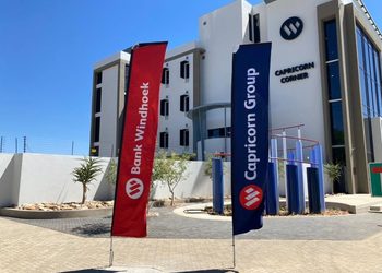 CAPRICORN5 - The Brief | Namibia's Leading Business & Financial News Modern corporate building with red Bank Windhoek and blue Capricorn Group flags in front of a clear sky.