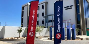 Modern corporate building with red Bank Windhoek and blue Capricorn Group flags in front of a clear sky.