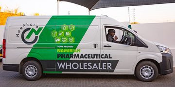 White promotional van for a Namibian pharmaceutical wholesaler with green branding and a driver waving from the cab window.