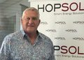Older man with gray hair in a patterned shirt stands in front of a HopSOL banner reading 'Smart Energy Solutions'.