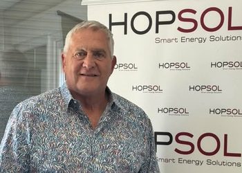 Older man with gray hair in a patterned shirt stands in front of a HopSOL banner reading 'Smart Energy Solutions'.