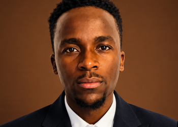 Nghuulili Martin Image - The Brief | Namibia's Leading Business & Financial News Close-up portrait of a Black man in a navy suit and white shirt, facing the camera against a brown studio backdrop.