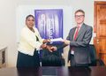 Two professionals shake hands while exchanging a document in an office, with a purple banner reading 'Fund Scholarships' in the background.