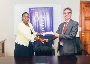Two professionals shake hands while exchanging a document in an office, with a purple banner reading 'Fund Scholarships' in the background.