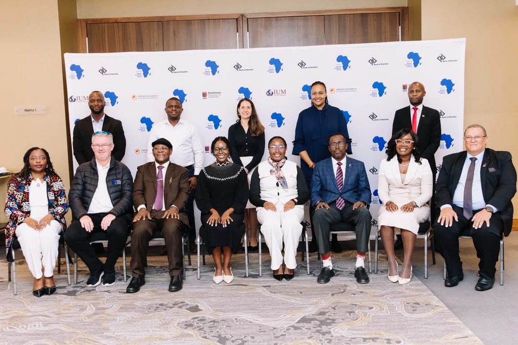 Group of 12 professionals in formal attire posing for a conference photo in front of a white backdrop with blue Africa map logos and event branding.