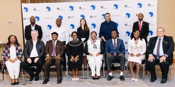 Group of 12 professionals in formal attire posing for a conference photo in front of a white backdrop with blue Africa map logos and event branding.
