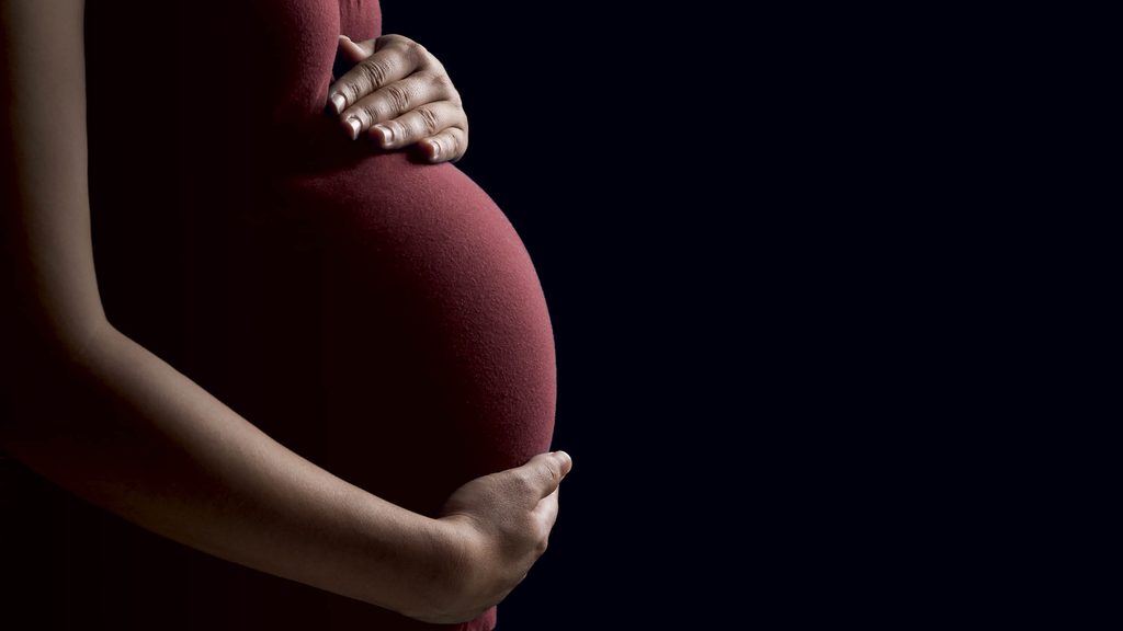 Pregnant person cradling their belly with both hands against a dark background.