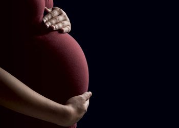 PREGNANT WOMEN - The Brief | Namibia's Leading Business & Financial News Pregnant person cradling their belly with both hands against a dark background.