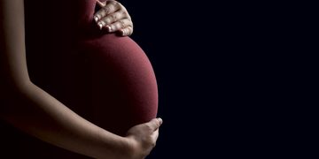 Pregnant person cradling their belly with both hands against a dark background.