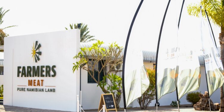 White storefront sign reading 'FARMERS MEAT' with 'PURE NAMIBIAN LAMB' text, palm trees, and tall promotional flags outside the shop.