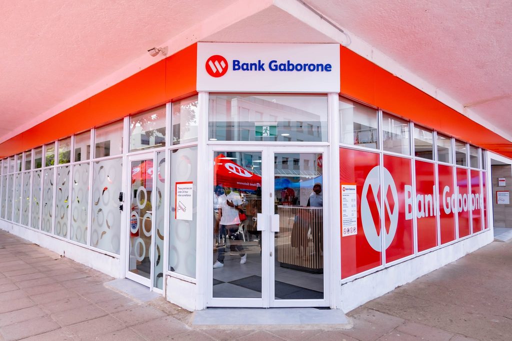 Exterior view of a Bank Gaborone branch with a glass storefront and bright red branding above the entrance, showing the logo and signage clearly.