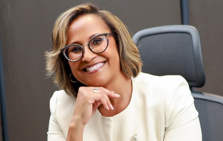 Kapena Tjombonde - The Brief | Namibia's Leading Business & Financial News Smiling woman with short hair and round glasses seated in an office setting, resting her chin on her hand.