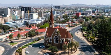 Aerial view of a city with a red-brick church at a roundabout center, surrounded by roads and palm trees.