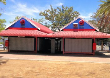 Two red-roofed NamPost post office kiosks with shuttered fronts in a sunny outdoor plaza, blue gable signs above.