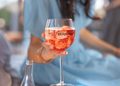 Person holding a stemmed glass of pink sparkling drink with the Bernini logo outdoors.