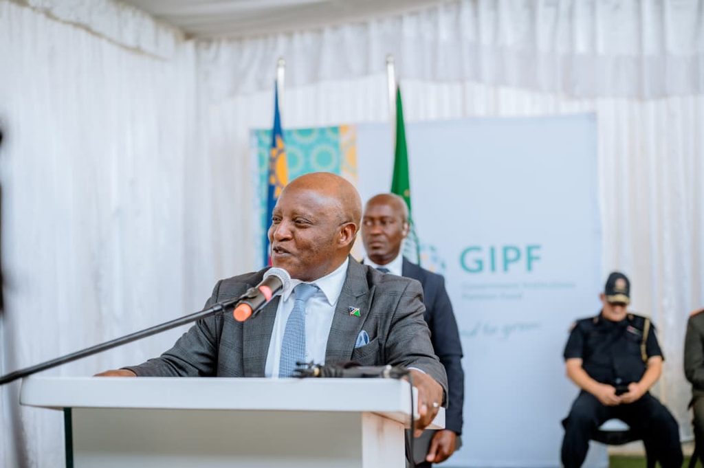 ELIJAH NGURARE8 - The Brief | Namibia's Leading Business & Financial News Public official in a gray suit speaks at a podium with a microphone; flags and a GIPF banner are in the background.