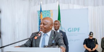 Public official in a gray suit speaks at a podium with a microphone; flags and a GIPF banner are in the background.