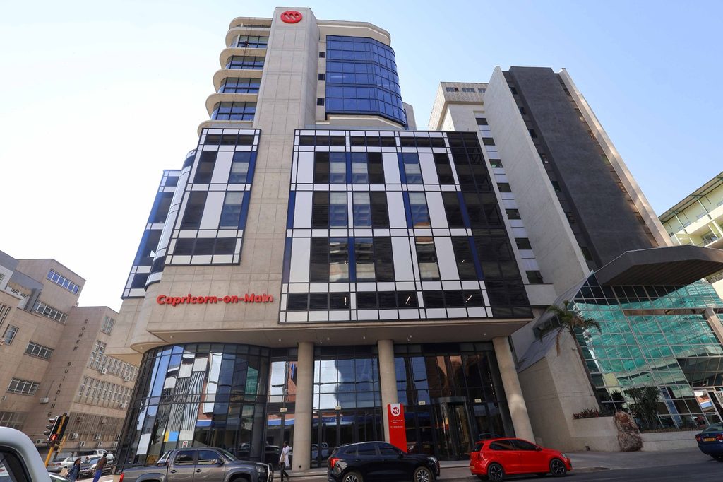 Modern office building with a striped glass facade, curved balconies on the left, and a red'Capricorn-on-Main' sign at ground level.