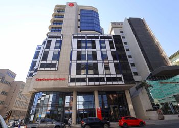 CAPRICORN BUILDING - The Brief | Namibia's Leading Business & Financial News Modern office building with a striped glass facade, curved balconies on the left, and a red 'Capricorn-on-Main' sign at ground level.