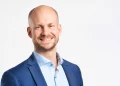 Smiling man in a blue blazer and light blue shirt against a white studio background (professional headshot).