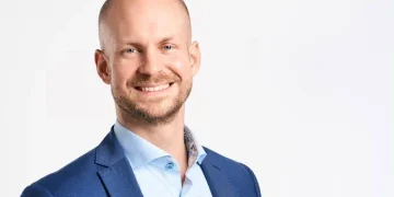 Smiling man in a blue blazer and light blue shirt against a white studio background (professional headshot).