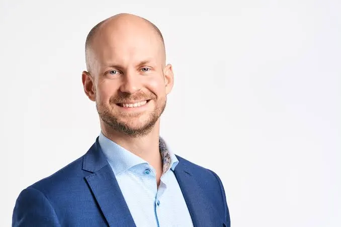 Smiling man in a blue blazer and light blue shirt against a white studio background (professional headshot).