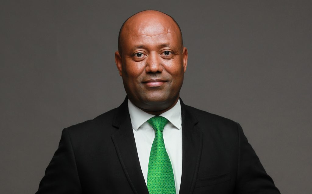 Biniam Ghirmatsion - The Brief | Namibia's Leading Business & Financial News Portrait of a man in a black suit and green tie, facing the camera against a gray backdrop.